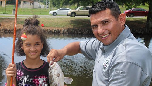 Wildlife officer holding fish this little girl caught with a cane pole