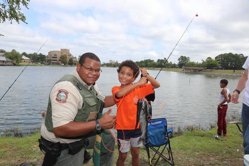 Wildlife officer and kid with catfish: Anglers are invited for fishing, prizes, food and fun at Lake Valencia Saturday. Photo by Mike Wintroath, AGFC.