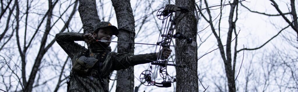 Man hunting deer on a tree stand with a bow and arrow.